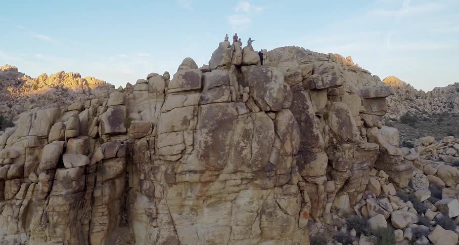 People standing and sitting on top of a boulder in a mountainous desert landscape