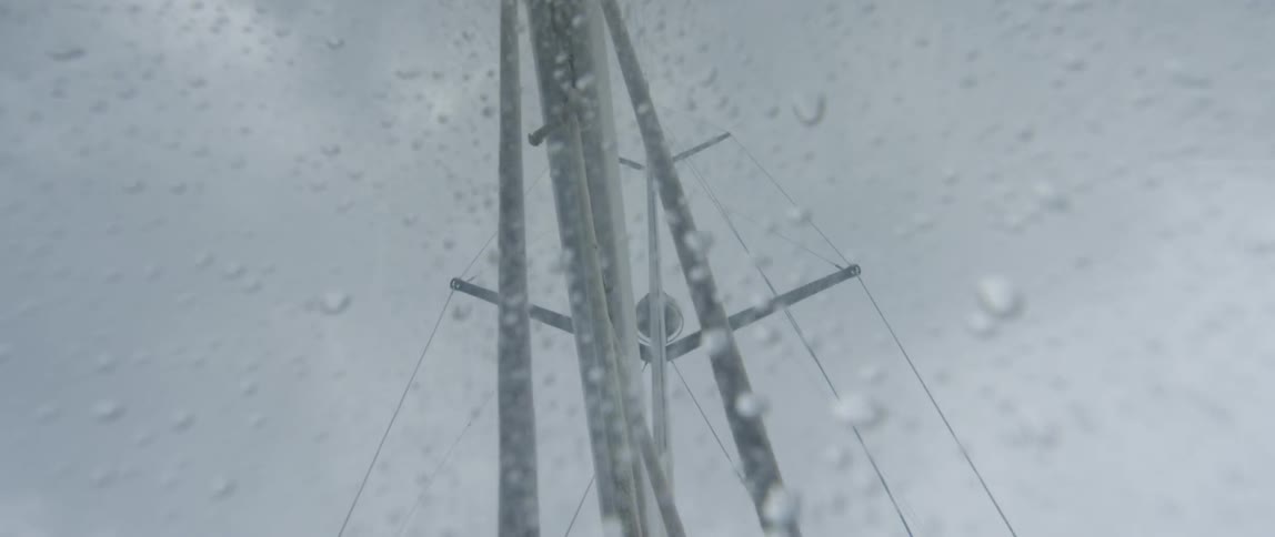 Rain drops gather on glass as a sailboat's mast sways in the wind