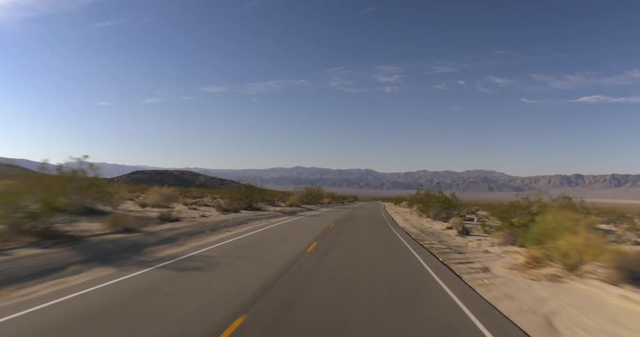 First person view of driving down a remote road headed towards mountains
