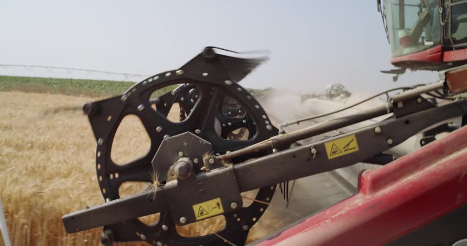 A tractor runs over wheat in a farm field