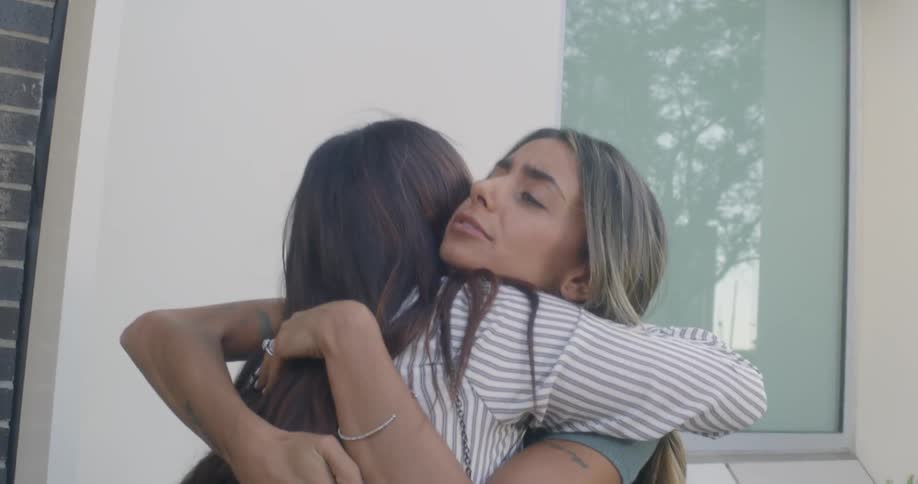 Women greet each other with hugs then sit at a restaurant patio table