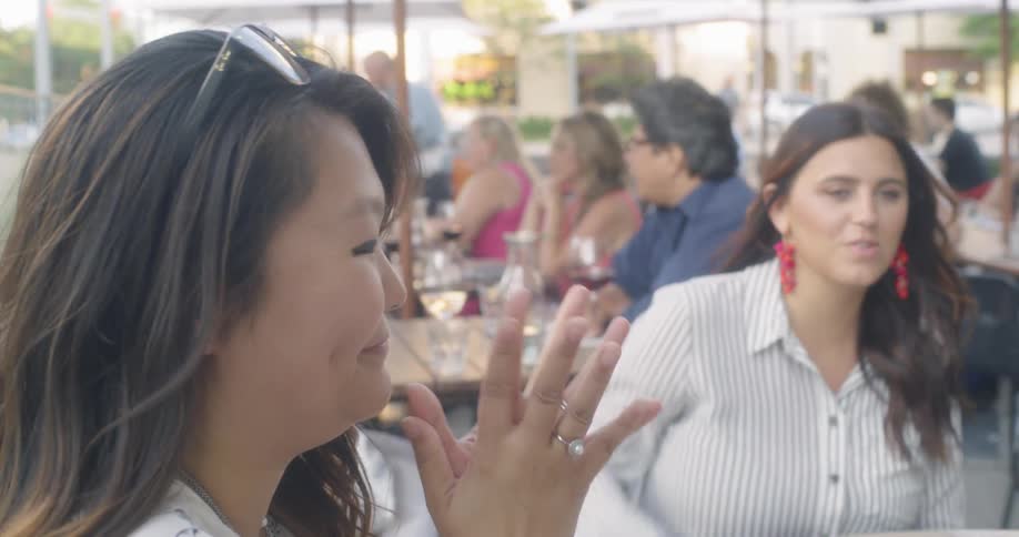 Women sitting outside at a restaurant gesture and smile as they talk