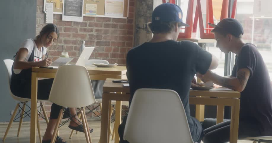 A woman sits at a cafeteria table working on her laptop