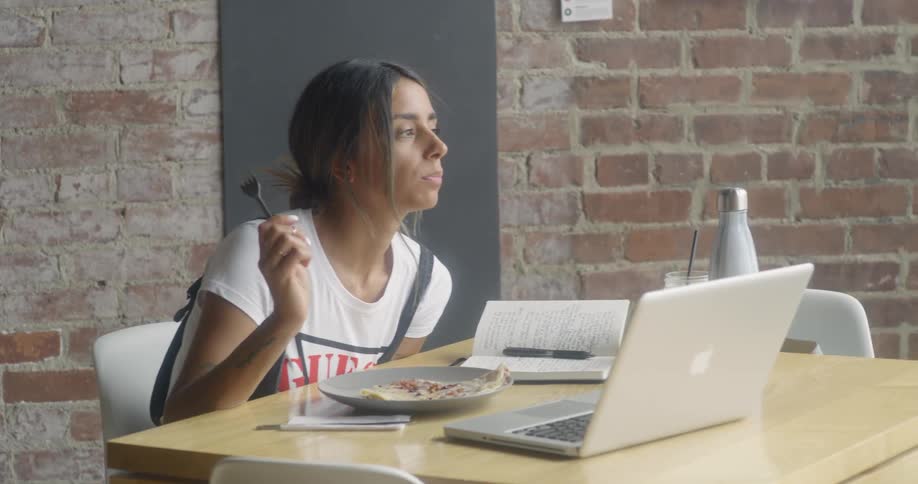A woman is eating her meal in front of her laptop