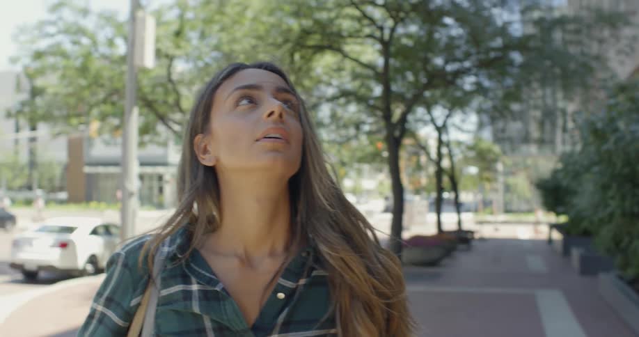 Woman stands on a city sidewalk and looks at a building