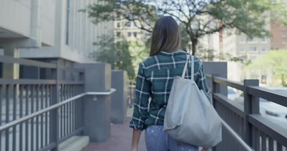 A woman carrying a bag walks up the entrance ramp to a building
