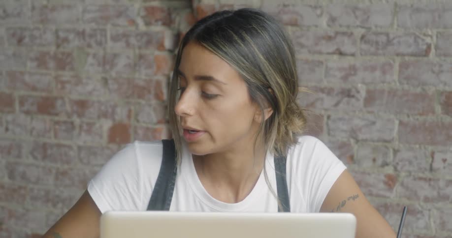 A woman sits at a table and uses a laptop