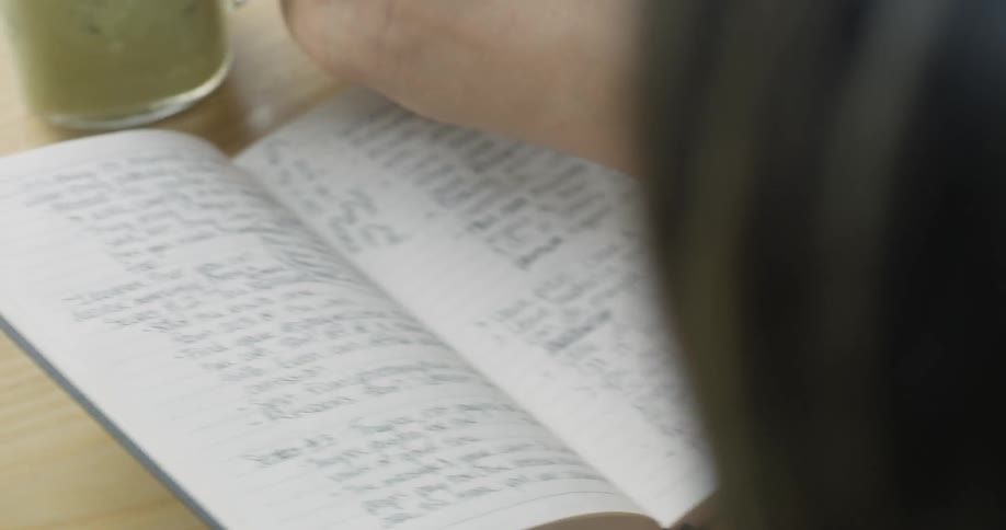 A woman drinks a smoothie while writing in a notebook