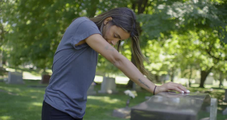 Woman stands and studies a gravestone