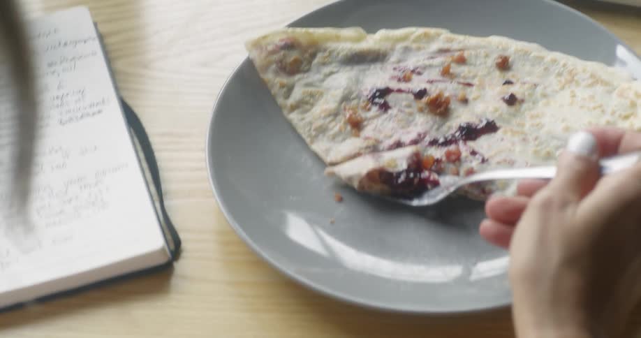 A woman eats a crepe at a table
