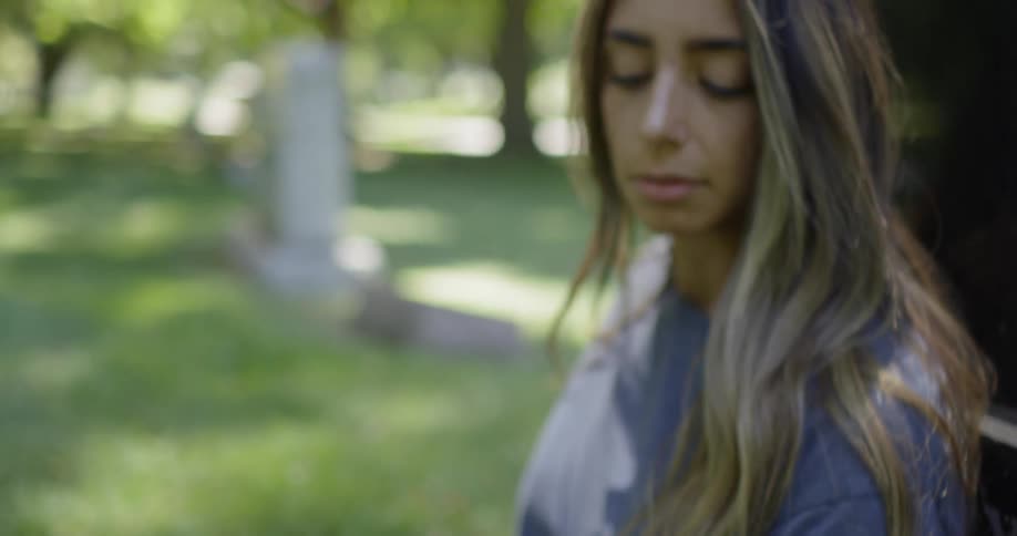 A woman rubs her hand over grass while sitting in a cemetery