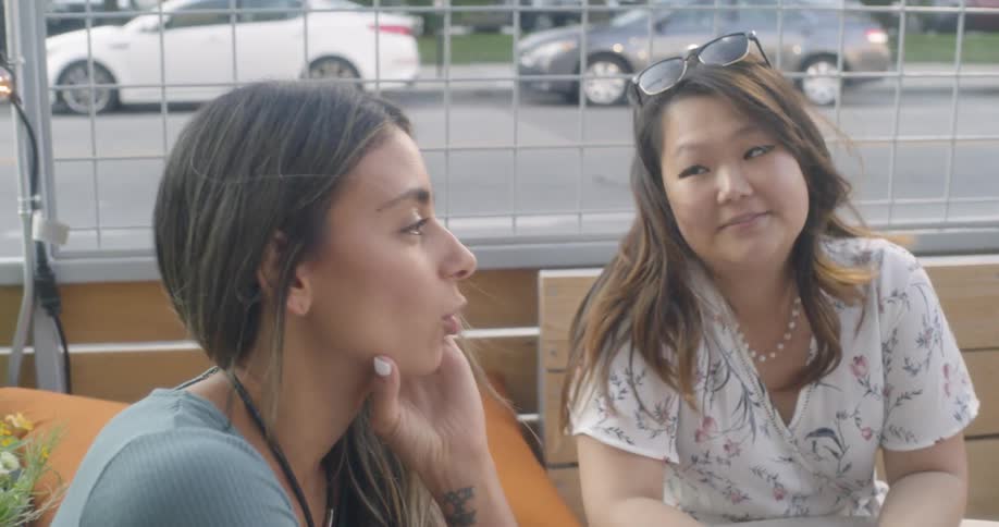 A group of female friends socialize as they sit at an outdoor table in a restaurant