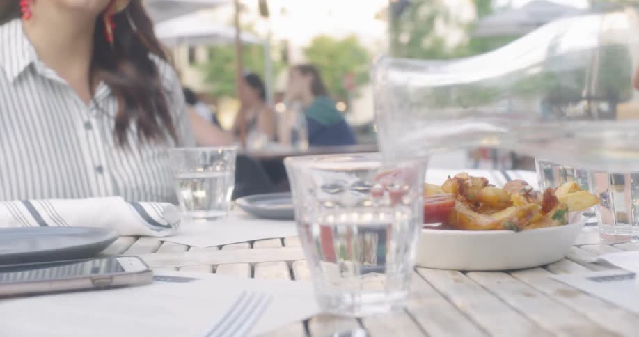 Water is being poured into a glass at an outdoor table