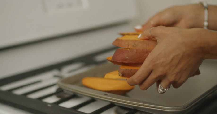 Woman places slices of sweet potato onto a baking sheet