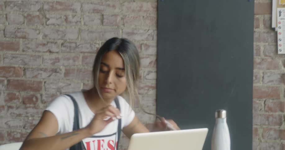 A woman sits down at a table with her laptop and notebook