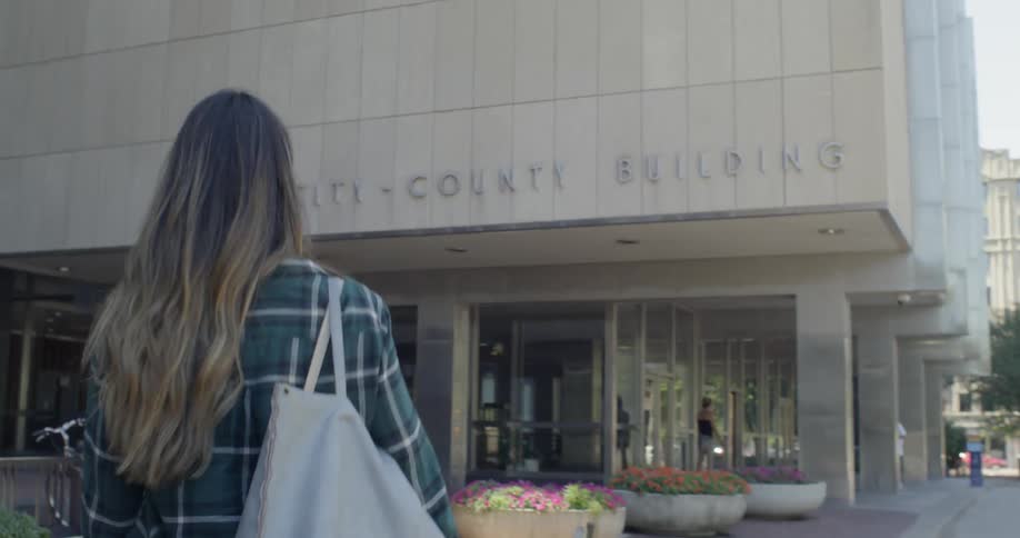 A woman is walking towards a building with a large bag on her shoulder