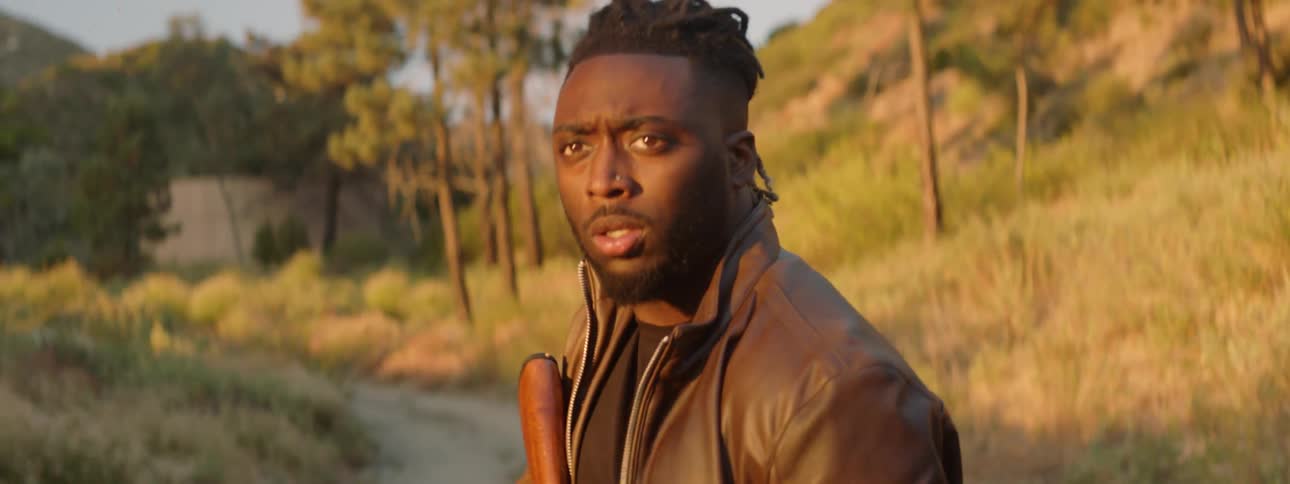 A man with a gun is standing on a dirt road and looks behind him