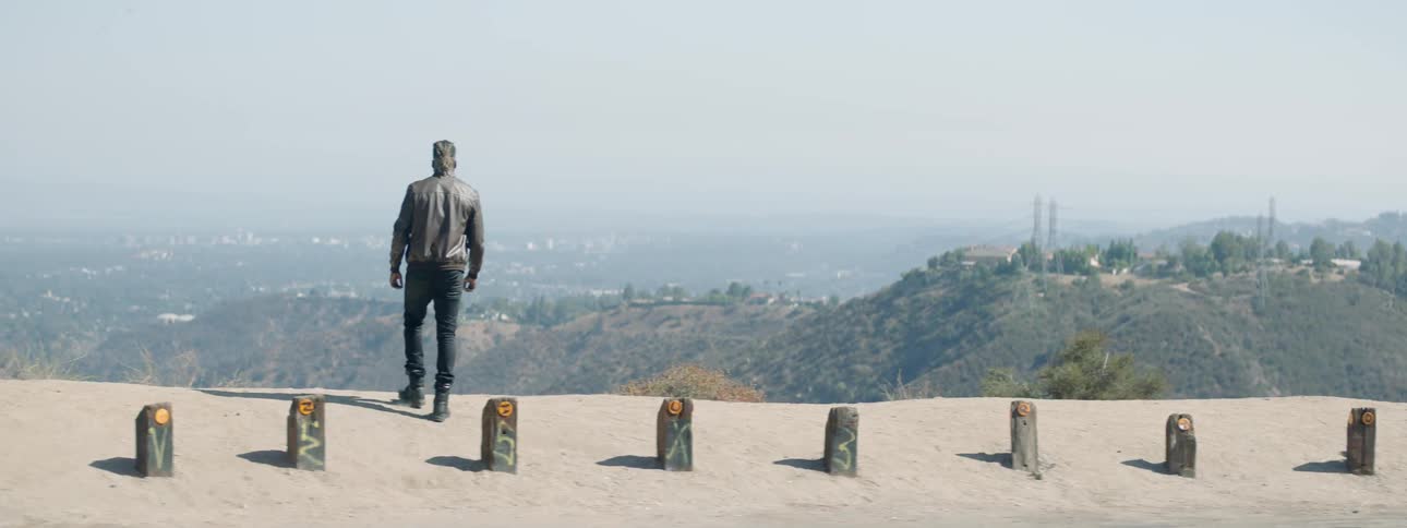 A man walks across a roadway to a lookout and takes in a view