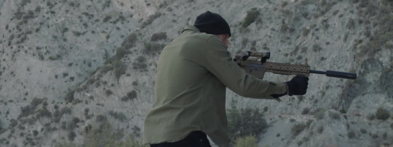 A man brandishes a rifle as he walks in a natural setting