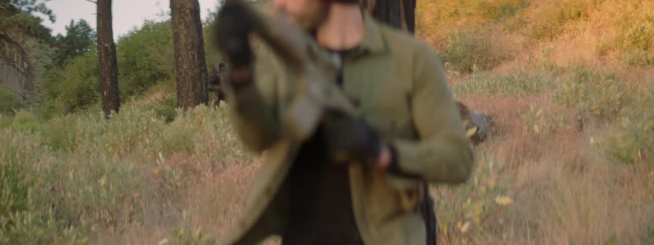 A man carrying a rifle is pursuing another man with a rival in a natural setting