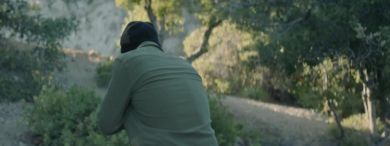 A man brandishes a rifle as he walks in a natural setting