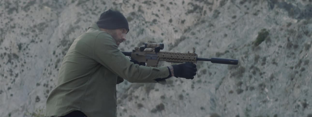 A man brandishes his scoped rifle as he searches for something in a natural setting