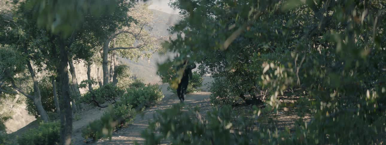 A man is hurrying along a dirt path carrying a rifle at the ready