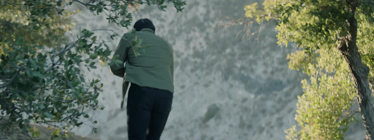 An armed man walks in the mountains and crouches with his gun