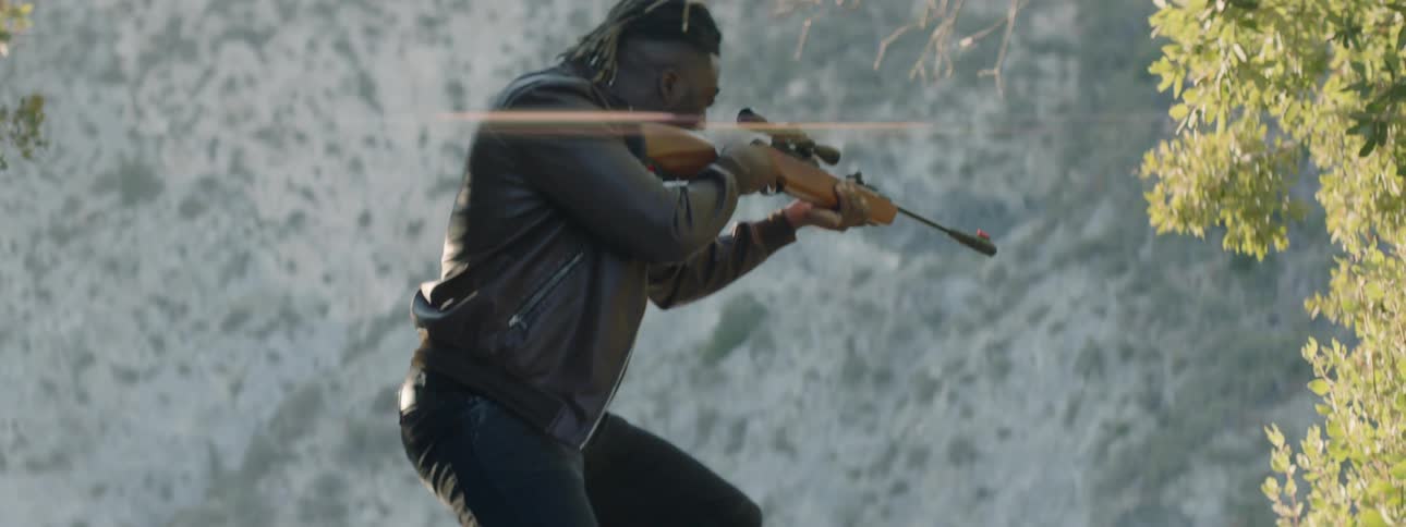 A man looks down the scope of his rifle as he stands in a natural setting