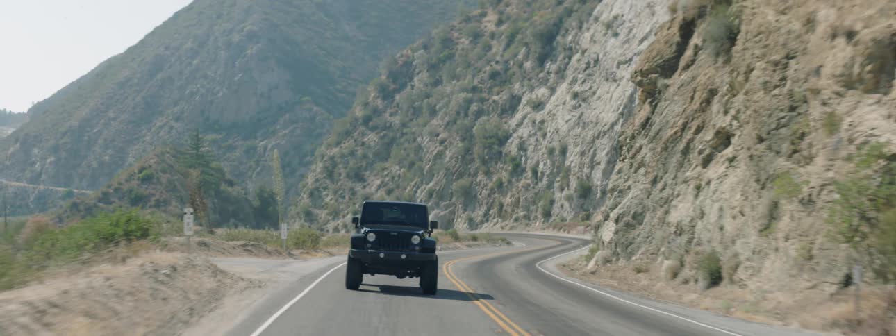 A jeep is being driven up a road in a mountain setting during the day
