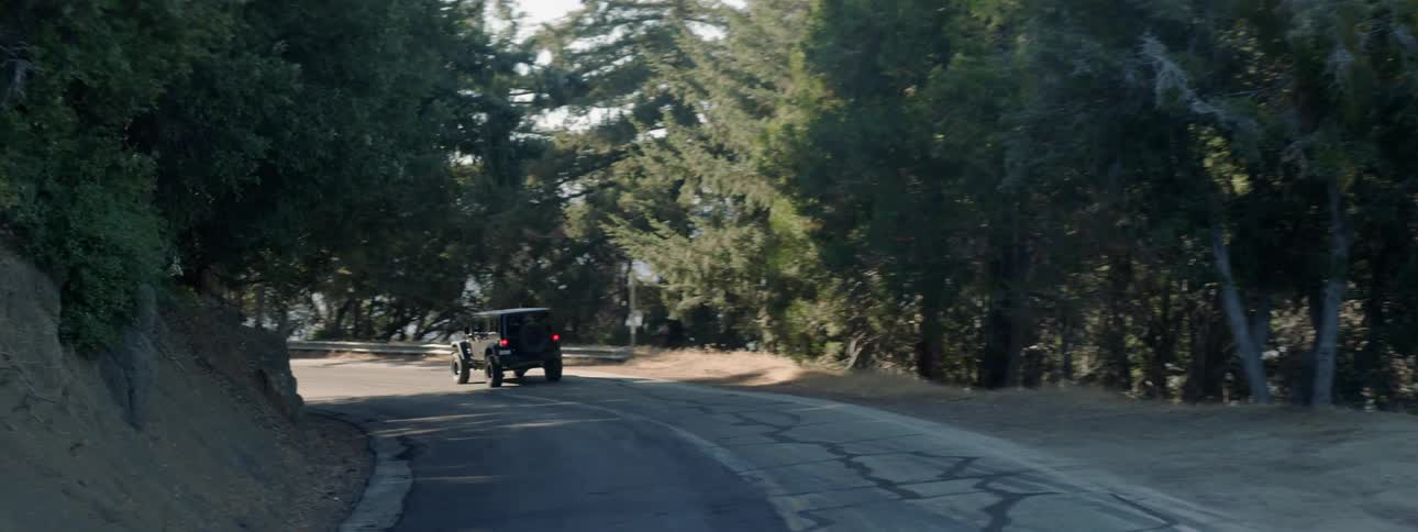 A jeep drives around a bend in a natural setting during the day