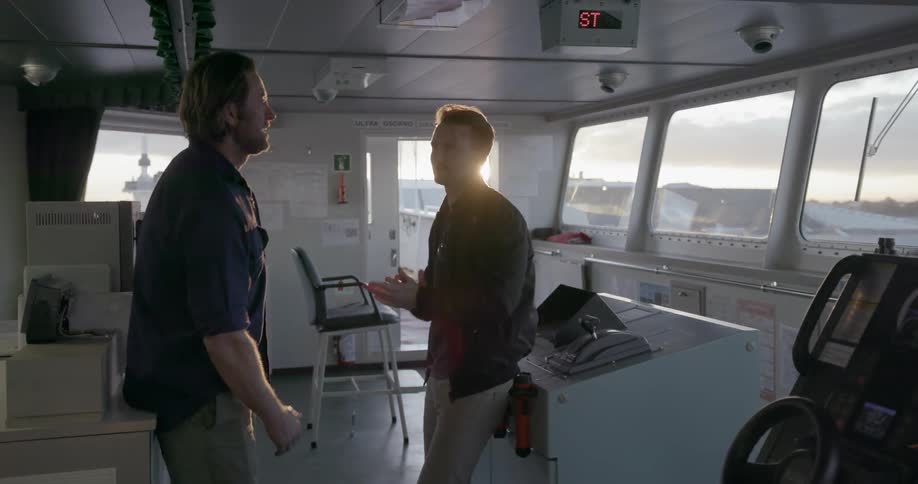 Two men talk and smile on a ship