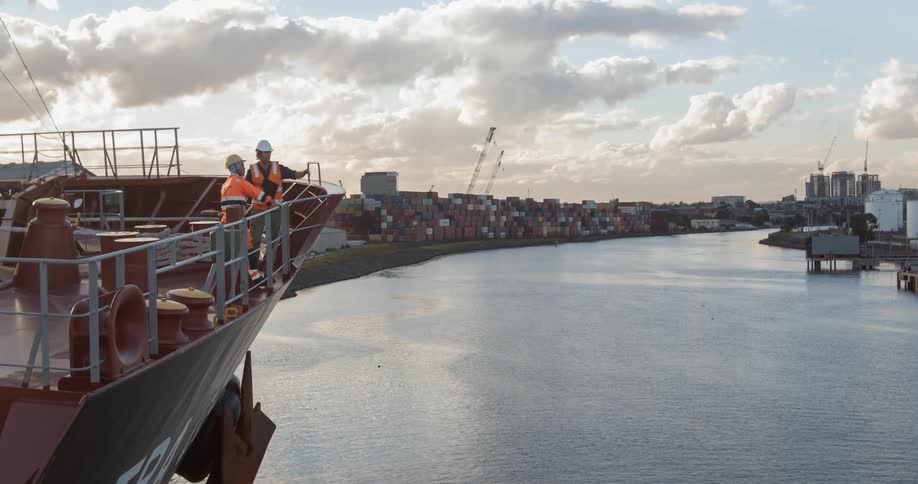 Two workers on a docked ship talk and point