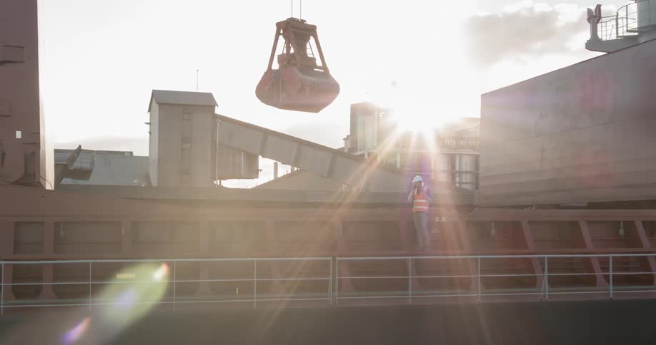 A construction worker stands beneath a crane on a ship