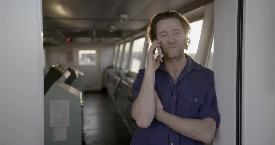 Man stands on a ship talking on a cell phone