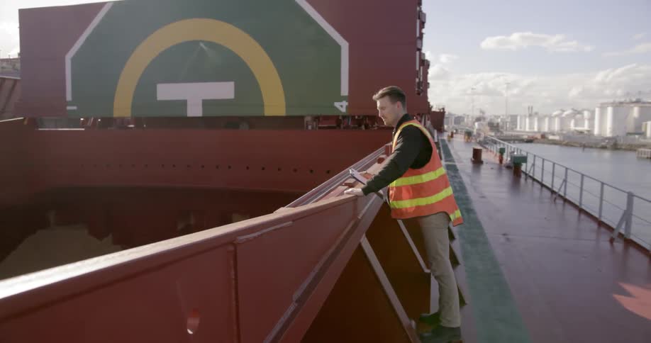 An inspector examines a large ship and writes on a clipboard
