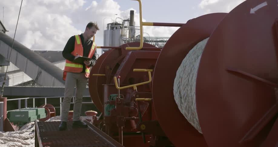 An inspector walks with a clipboard while examining a ship