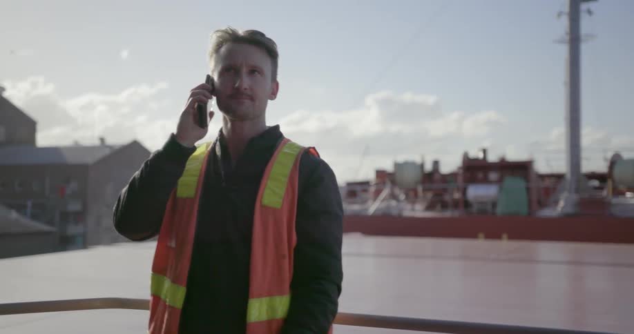 Man in an orange vest stands next to a railing talking on a phone