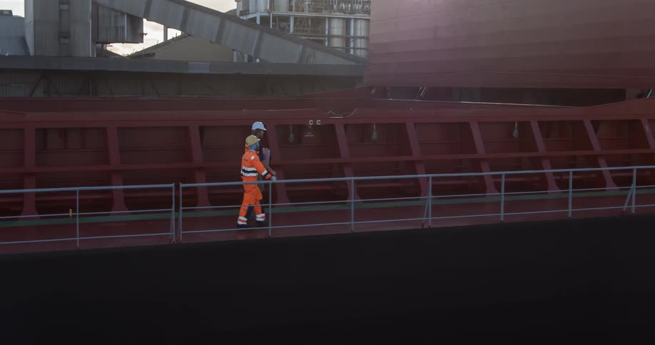 Two workers with helmets walk on a large ship