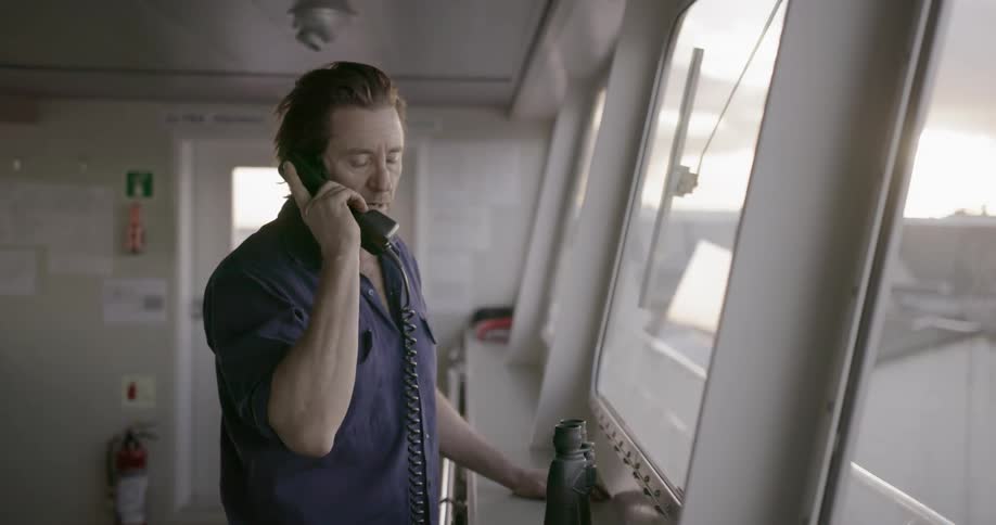 A man in blue talks on a ship phone