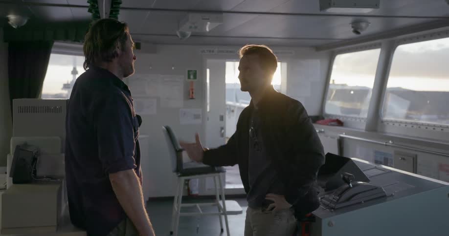 Two men talk on a ship on a sunny day