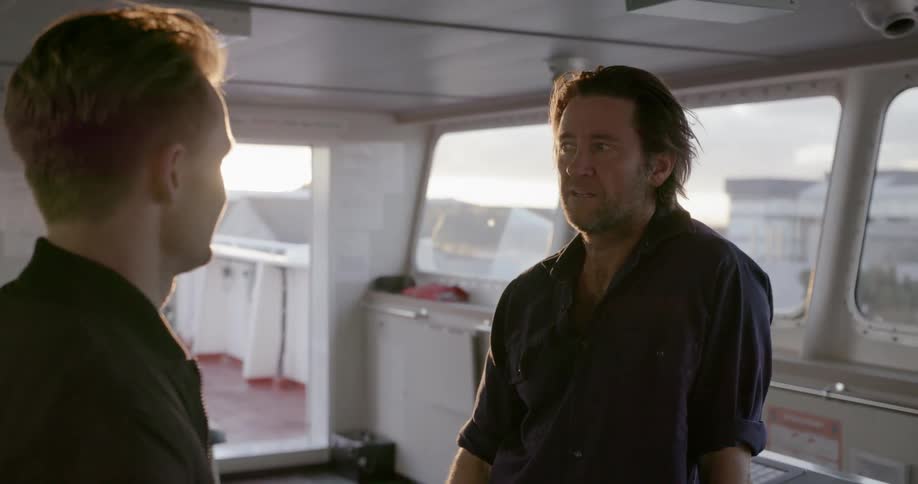 Two men talk while standing on a ship at sunset