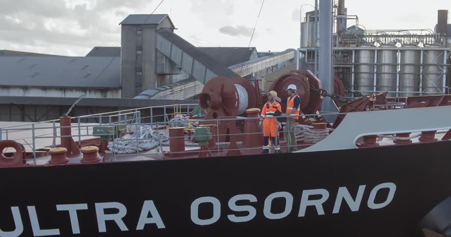 Two men stand on the deck of a ship having a discussion during the day