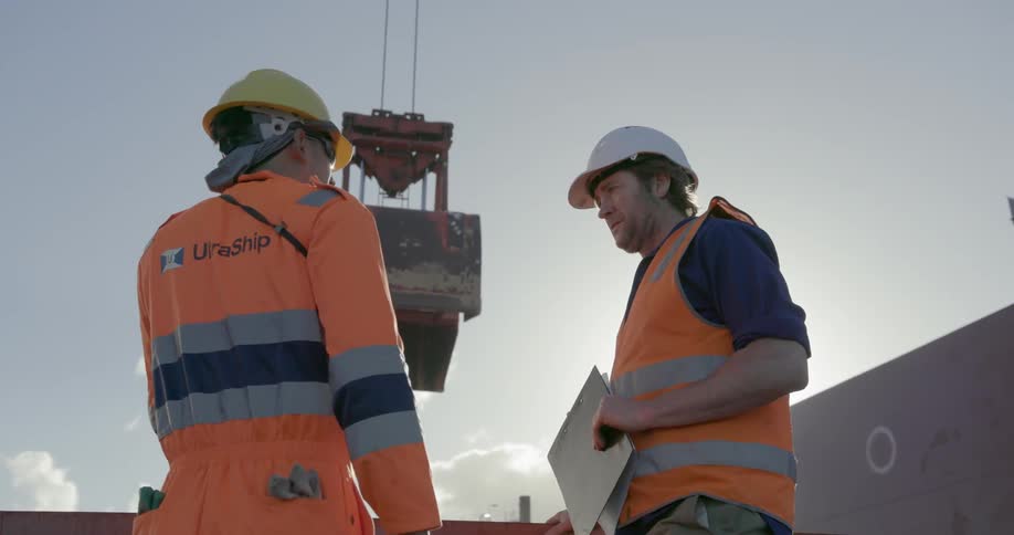 Two construction workers talk near a crane
