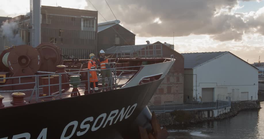 Two men stand on the deck of a ship having a discussion during the day