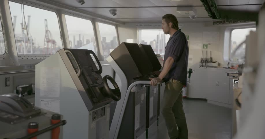 A man stands on the bridge of a ship watching a control panel