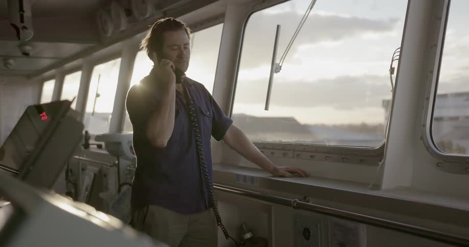 Man stands on a ship talking on a cell p hone
