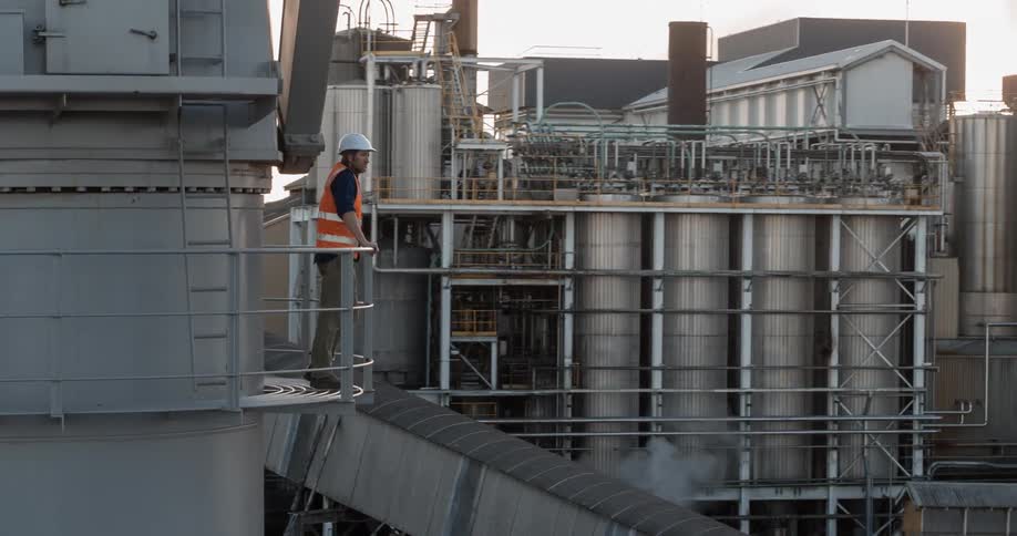 A construction worker leans against a rail at a factory