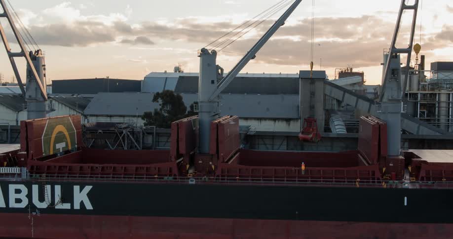 A construction worker stands beneath a crane on a ship at sunset