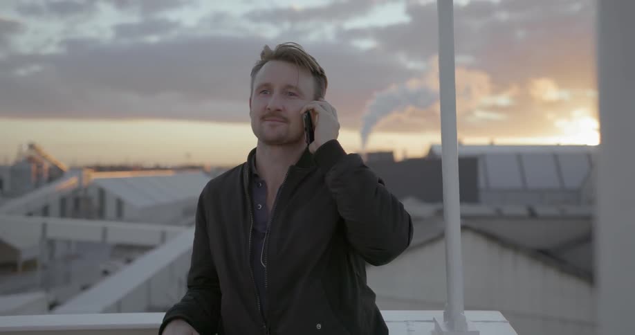Man talks on a cell phone in a city at sunset